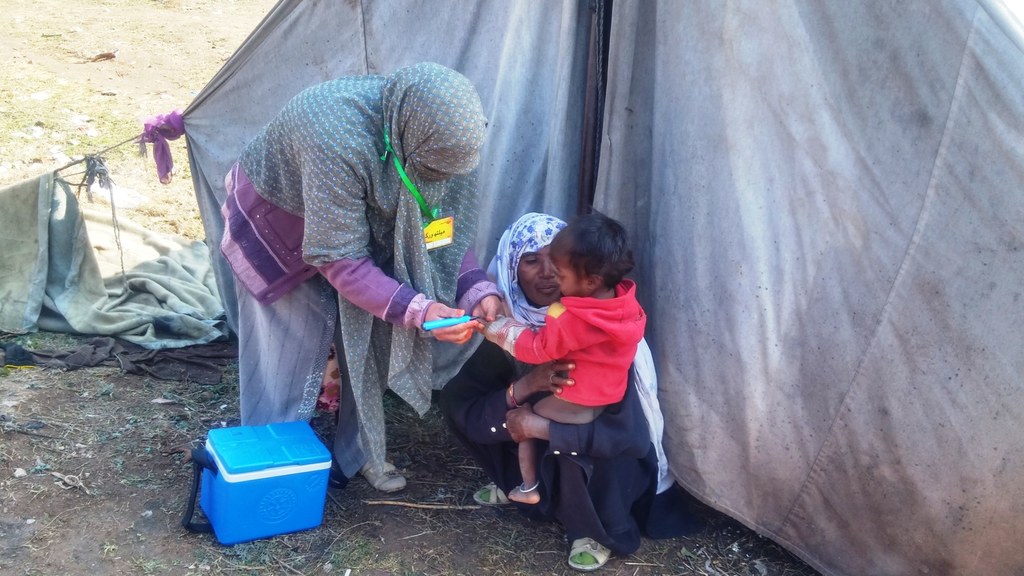 A frontline polio vaccinator administering polio drops to a child during a vaccination campaign in Pakistan.