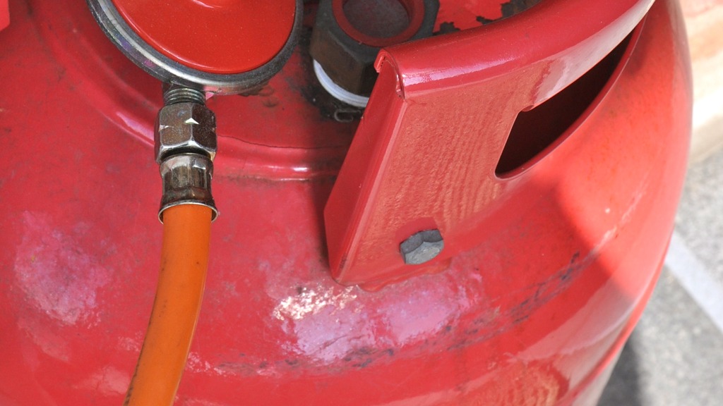 Red LPG gas cylinder with regulator and hose.