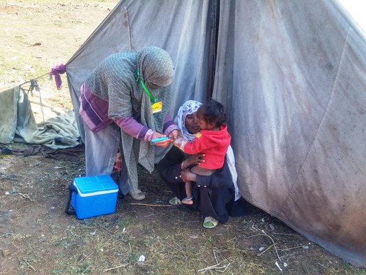 Polio vaccination worker with a vaccine cold box giving drops to a child during a polio campaign in Pakistan