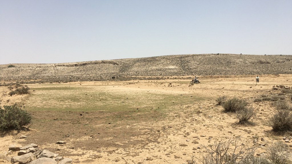 Arid hills and open ground in Khuzdar district, Balochistan, with motorcyclists crossing the plain