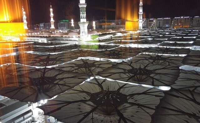 The Prophet's Mosque in Madinah at night with its courtyard umbrellas open, the destination of the pilgrims' journey