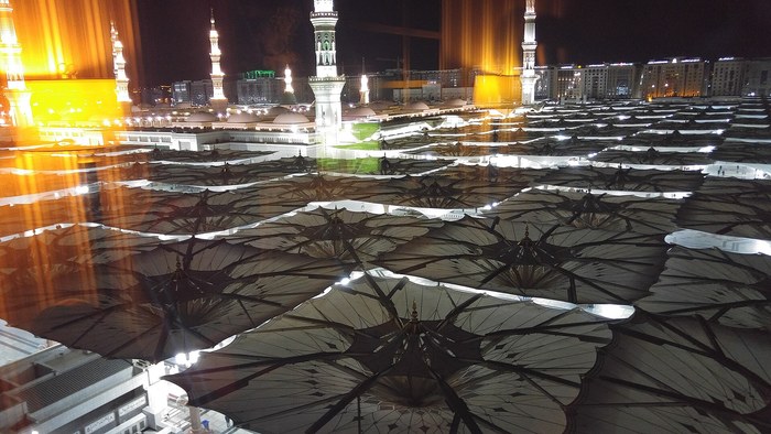 The Prophet's Mosque in Madinah at night with its courtyard umbrellas open, the destination of the pilgrims' journey