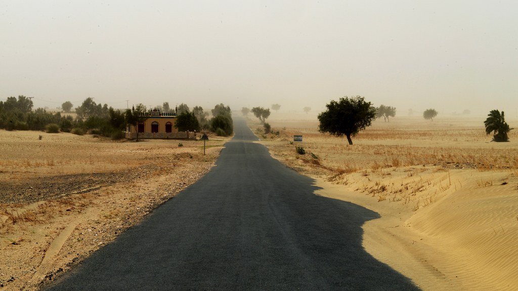 A road through the Thal Desert in Punjab disappearing into a sandstorm, with sand drifting across the asphalt