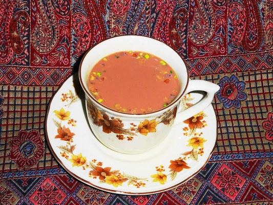 A cup of Kashmiri pink chai topped with crushed nuts, served on a floral saucer over a patterned Kashmiri cloth