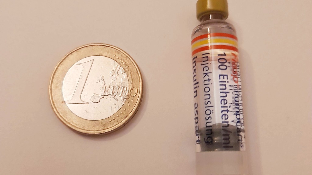 An insulin vial beside a one-euro coin for scale.