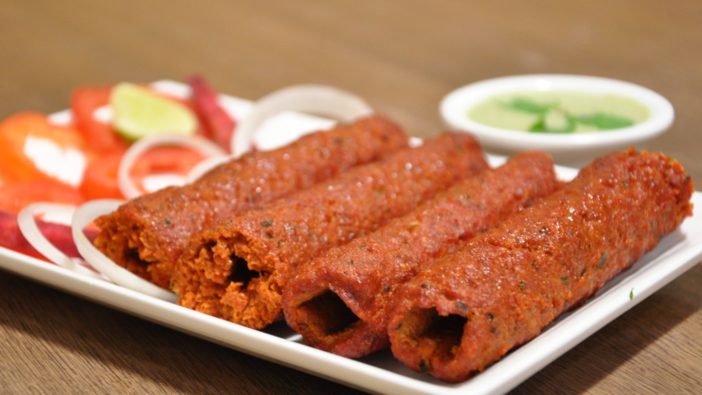 A plate of mutton seekh kebabs served with onion rings, tomato, lemon and green chutney, the dish prepared using this seekh kebab recipe