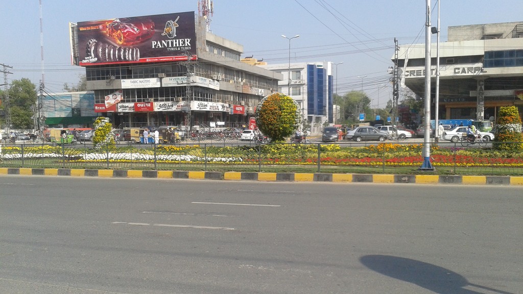 Main Boulevard in Gulberg, Lahore, with commercial buildings near Hafeez Centre across the flower-lined central reservation