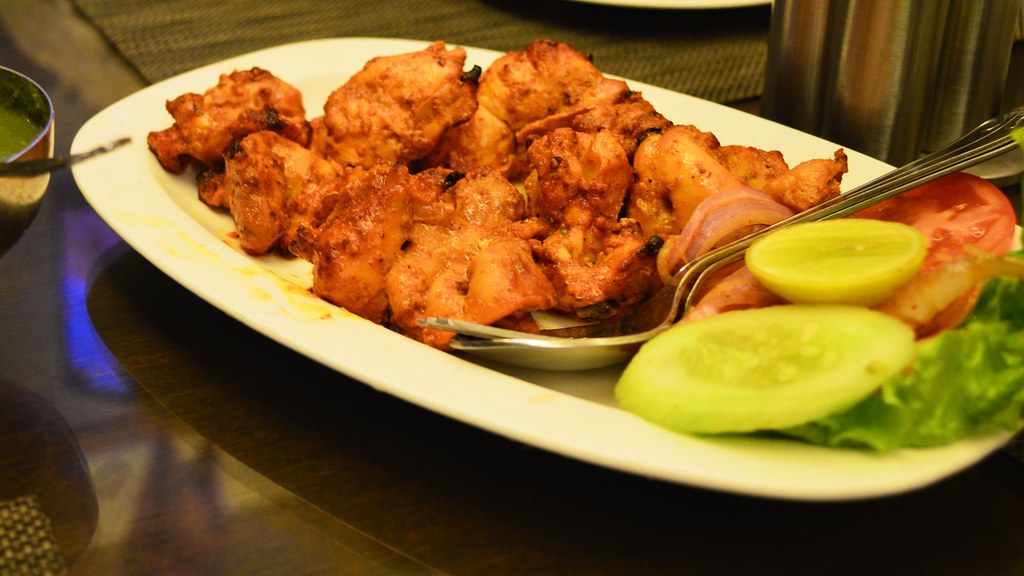 A plate of chicken tikka with lemon wedges, cucumber, tomato and onion rings, the dish prepared using this recipe