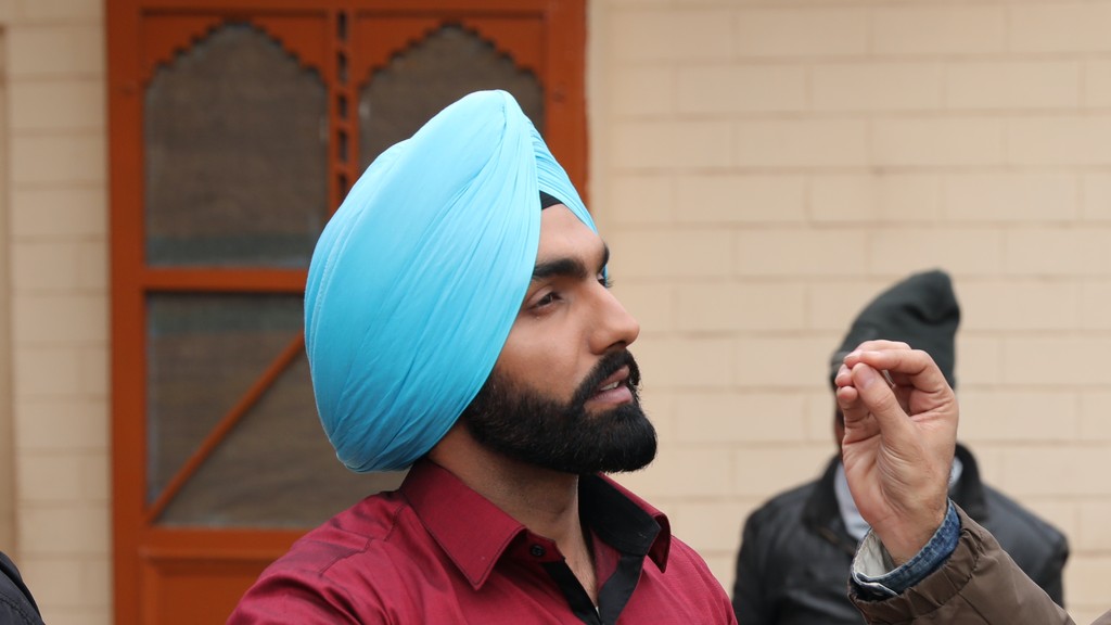 Punjabi singer and actor Ammy Virk, in a blue turban and red shirt, talking on a film set