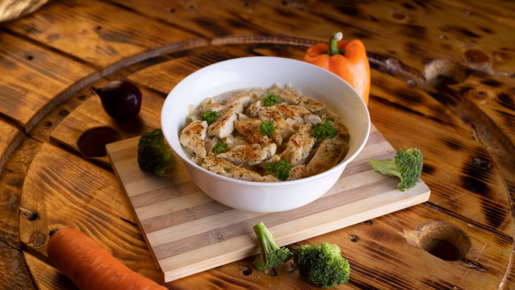 A bowl of homemade chicken soup served on a wooden board with fresh herbs