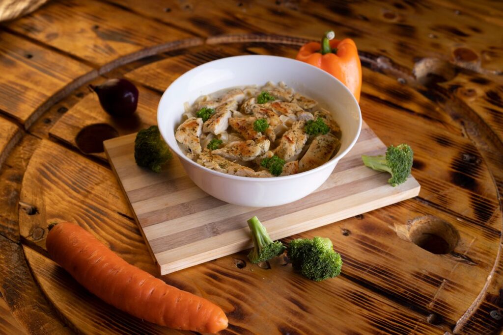 A bowl of homemade chicken soup served on a wooden board with fresh herbs