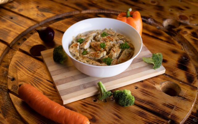 A bowl of homemade chicken soup served on a wooden board with fresh herbs