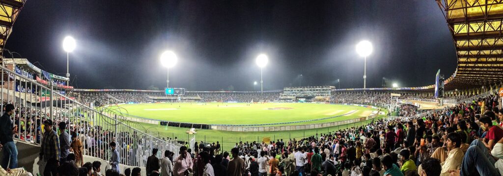 A packed cricket stadium under floodlights during a night match