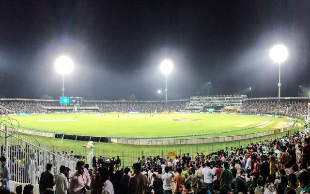A packed cricket stadium under floodlights during a night match