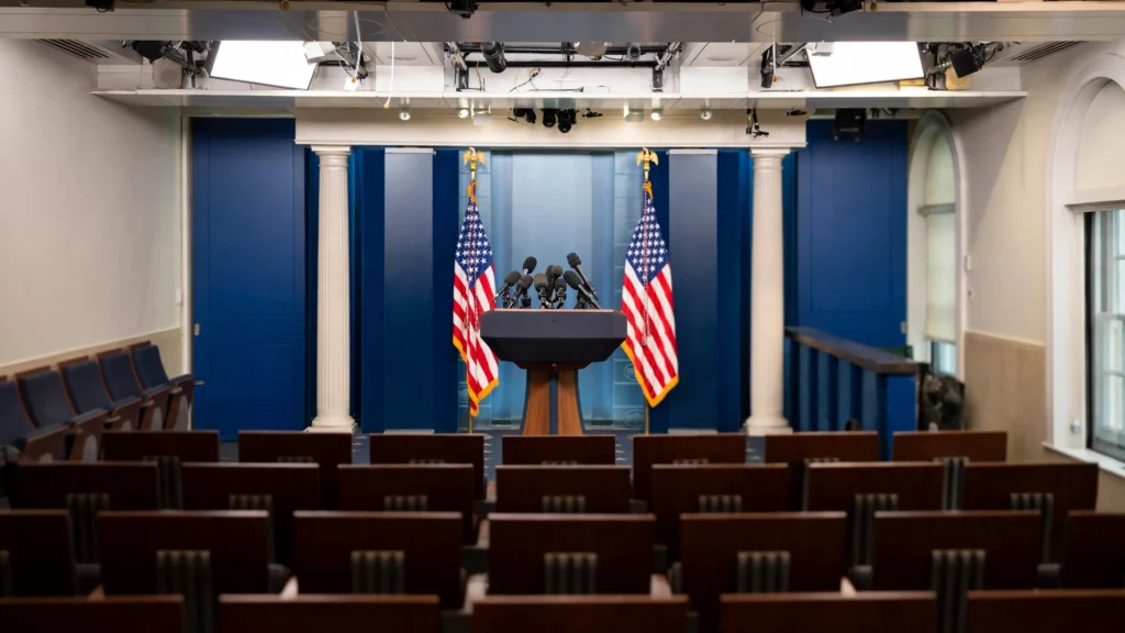 Podium with microphones in the White House press briefing room with American flags